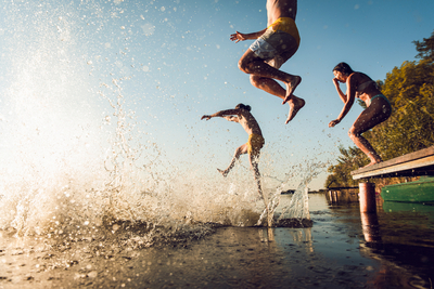 Drei Personen springen von einem Steg in einen See
