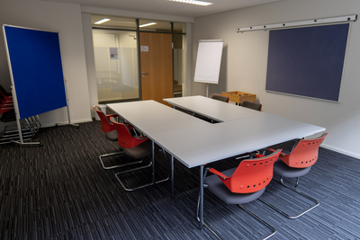 Gruppenraum für Seminarteilnehmer mit weißen Tischen und roten Stühlen, einem Flipchart und einer Tafel