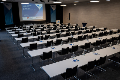 Blick in den Großen Konferenzsaal mit Tisch- und Stuhlreihen sowie der Folie einer Powerpoint-Präsentation auf dem großen Display 