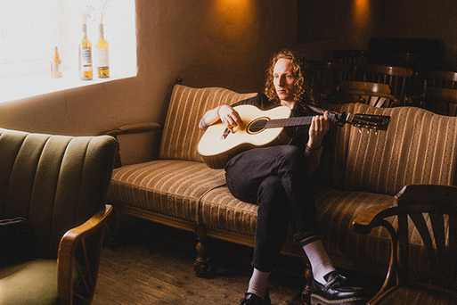 Moritz Herrmann sitzt mit Gitarre auf einer Couch.