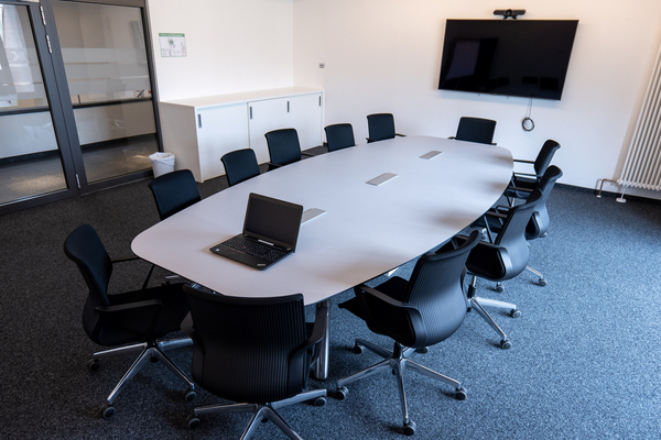 Kleiner Konferenzraum. Foto: BZK Der kleine Konferenzraum im BZK. Im Raum ein ovaler Tisch mit Bestuhlung und an der Wand ein Bildschirm.